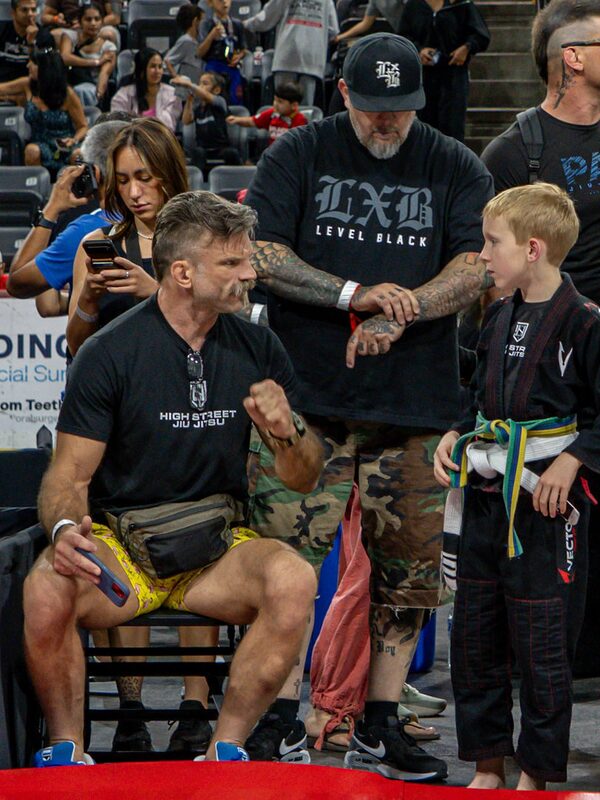 Brendon sits matside at a tournament coaching a young competitor between matches