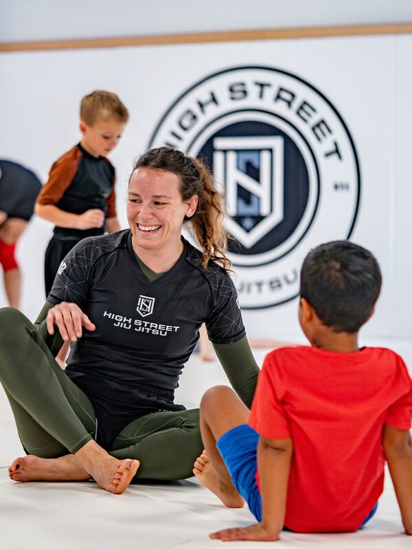 Karla sits on the mats smiling with the kids class gathered around her
