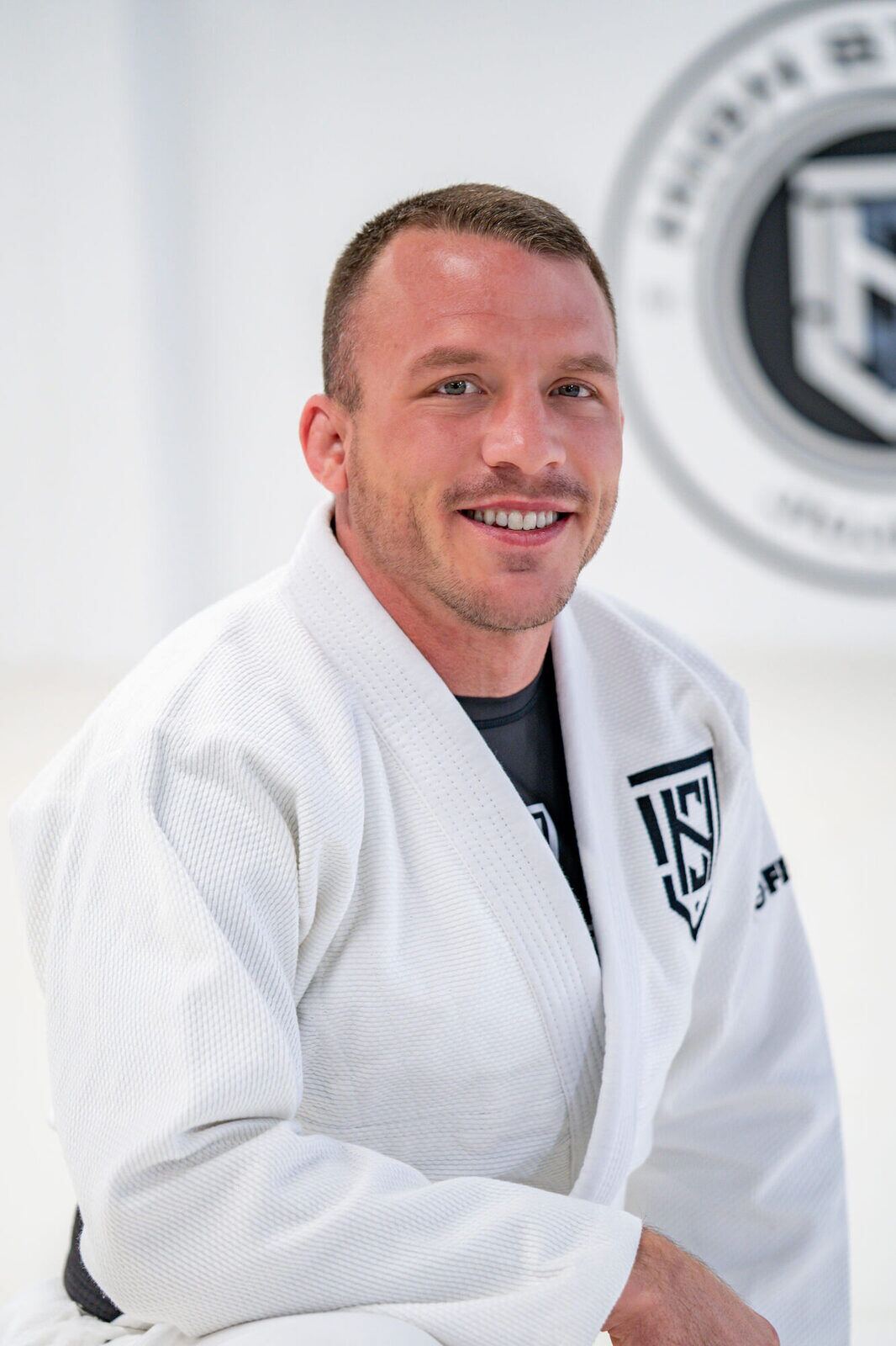 Coach Frank Ramsey smiling in a white gi beneath the High Street seal