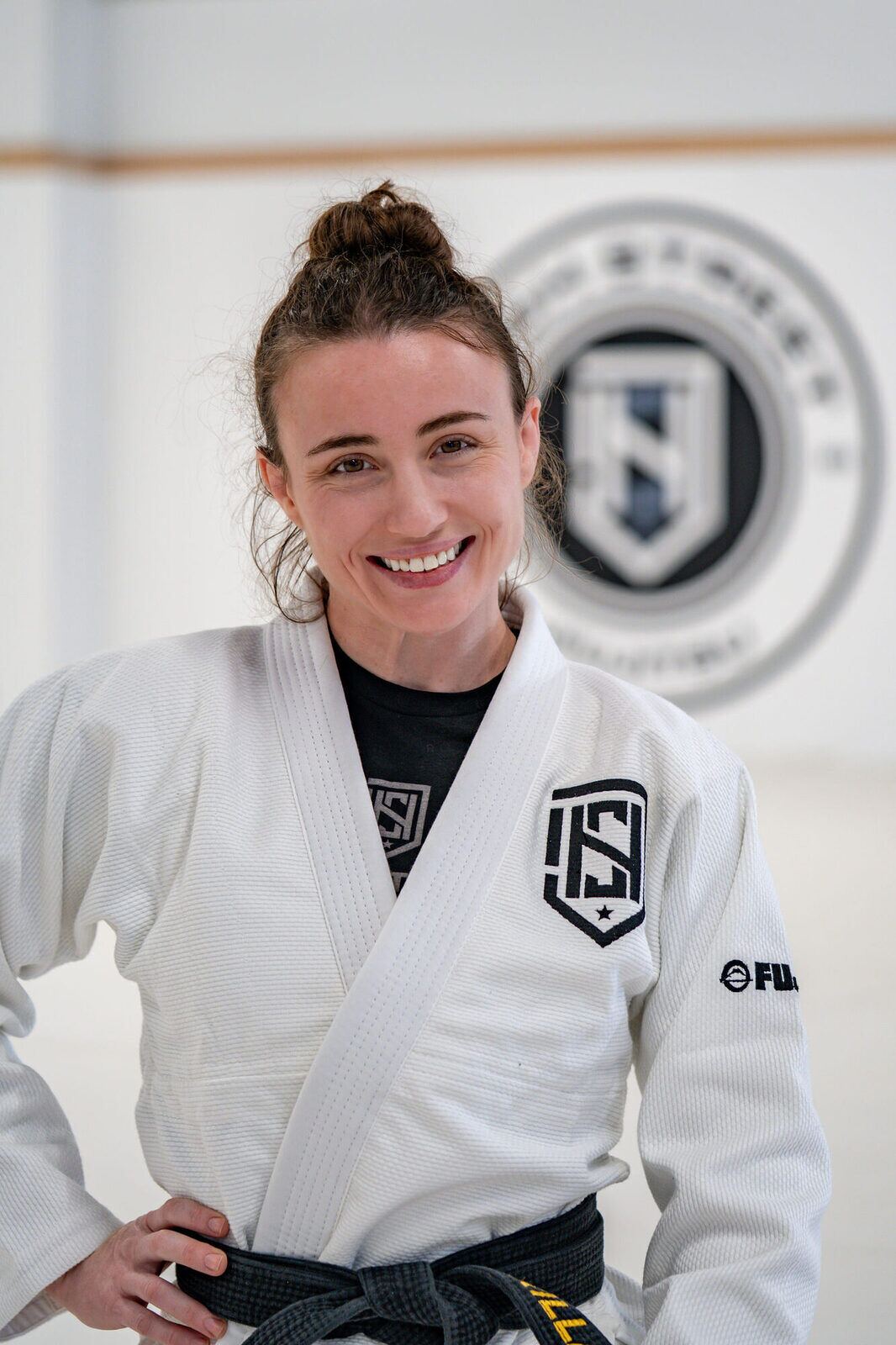 Coach Makilla Jones smiling in a white gi and black belt beneath the High Street seal