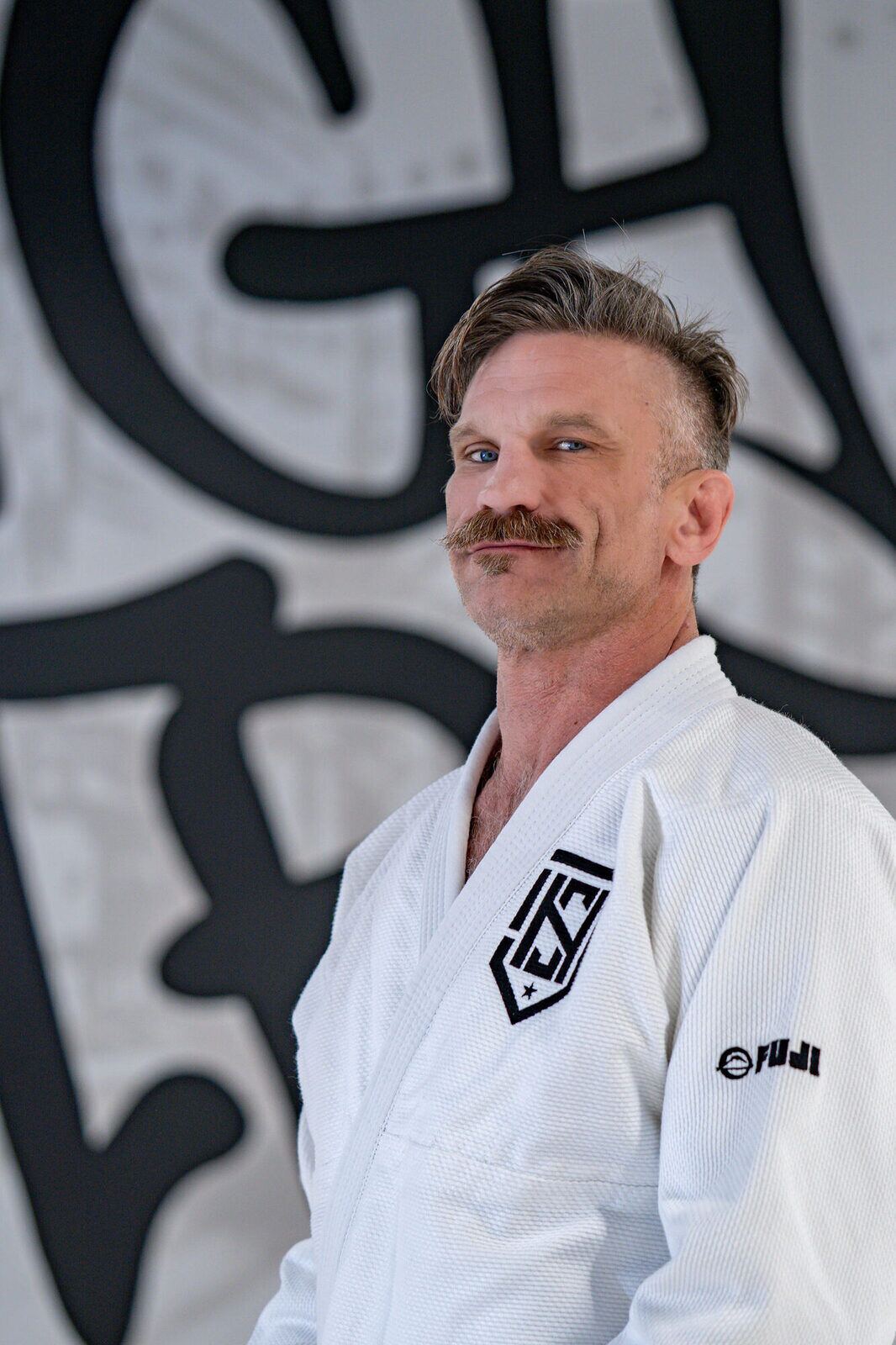 Coach Brendon Tierney in a white gi and black belt against the High Street mural