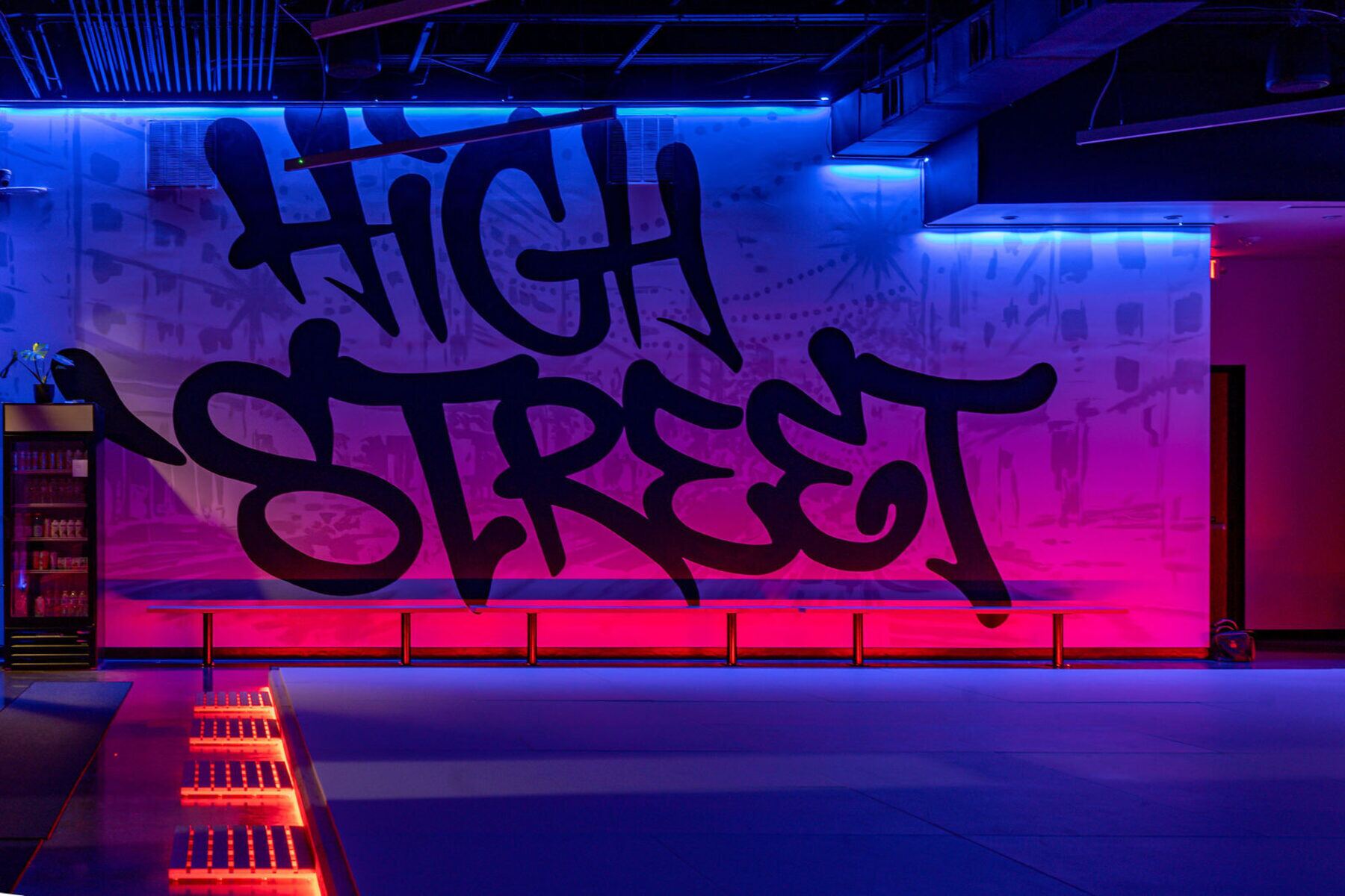 The academy's mural wall glowing under pink and blue neon