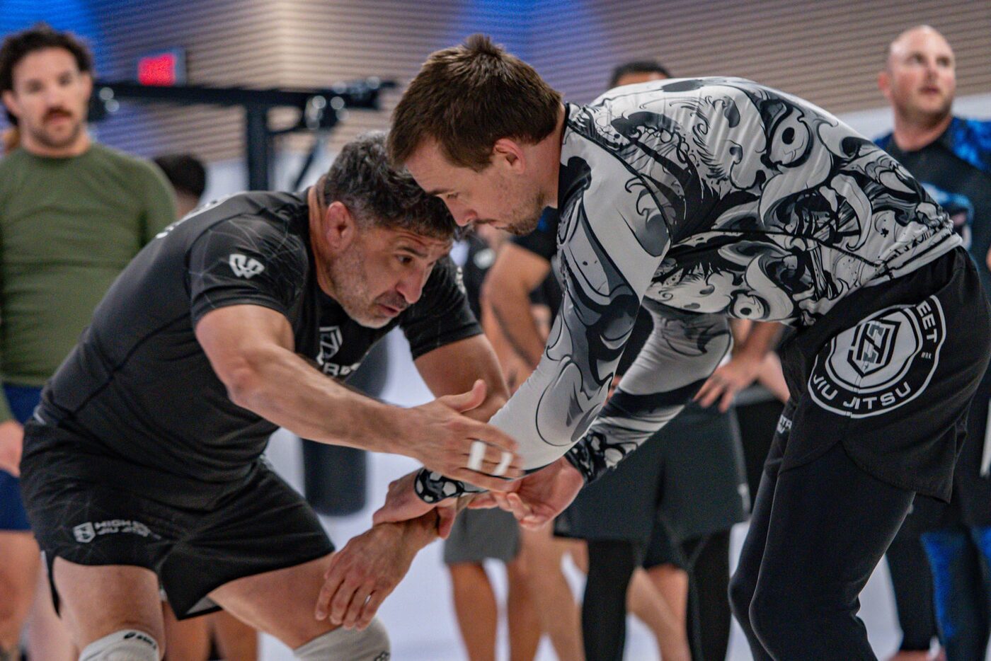 Three no-gi grapplers work a hand-fighting drill on the mats with the class around them