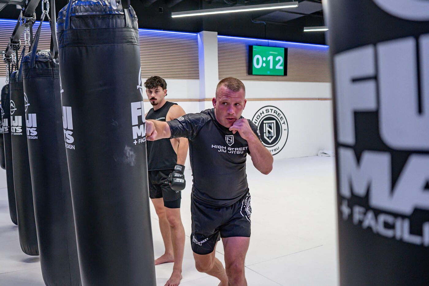A striker in gloves drives a punch into a heavy bag between the rows of bags